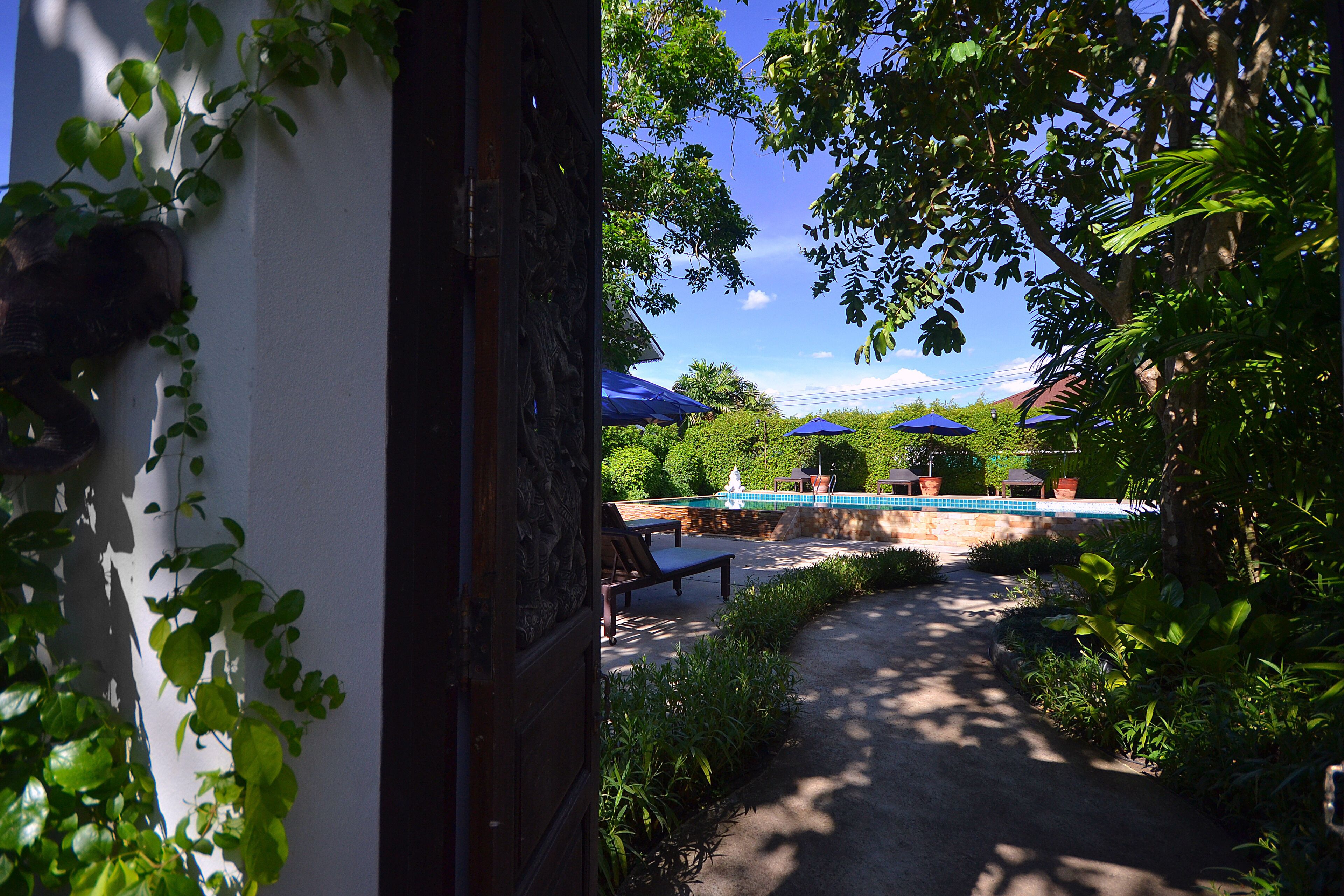 A pathway leading to a pool area with blue umbrellas and lounge chairs.