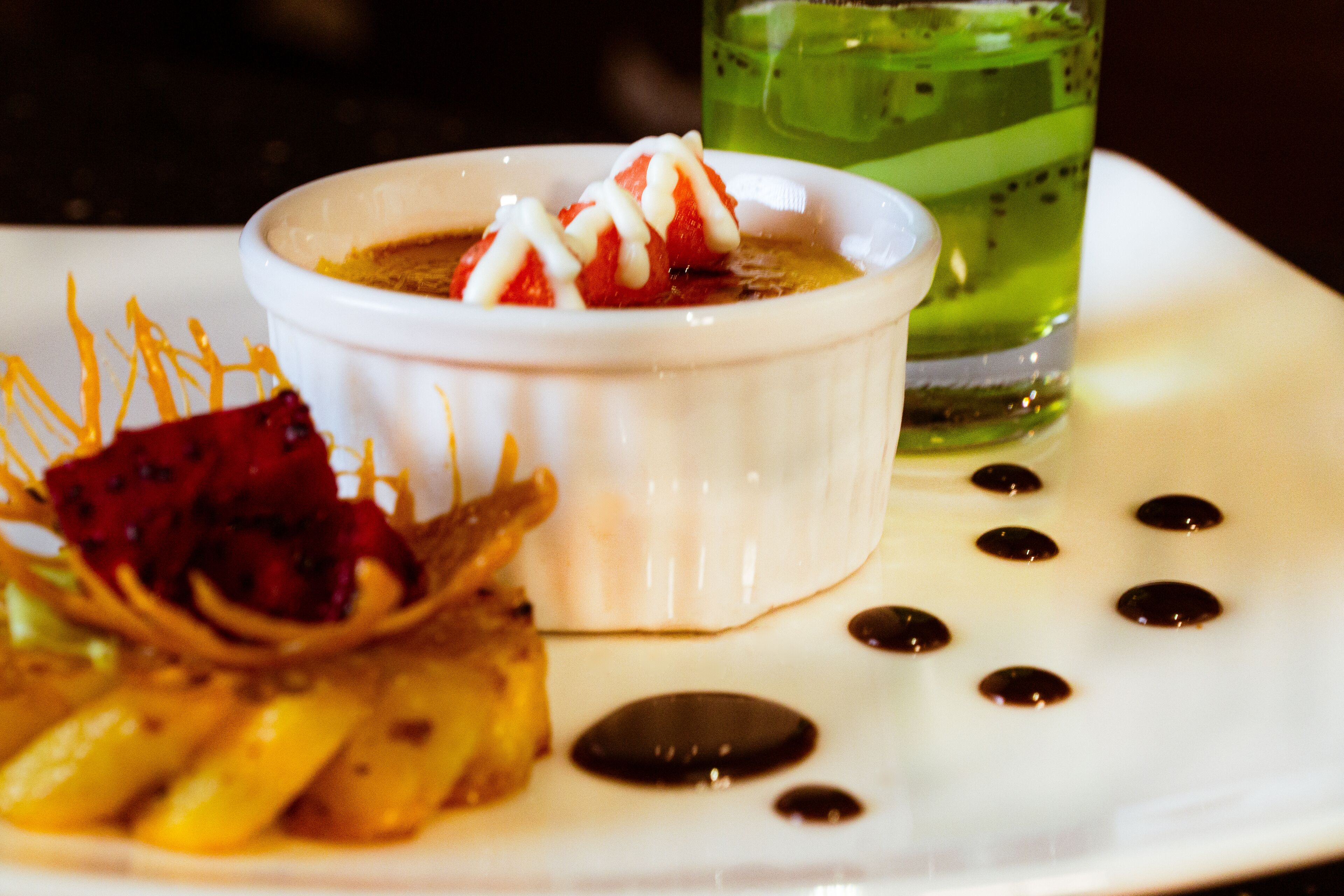 Ein Dessertteller mit einer weißen Schale, gefüllt mit Dessert, belegt mit Erdbeeren und Schlagsahne, dazu ein Drachenfruchtstück und eine Bananenscheibe.