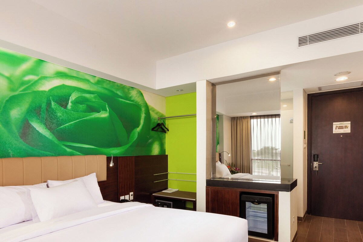 A hotel room with a large bed, a bathroom with a mirror, and a green wall.