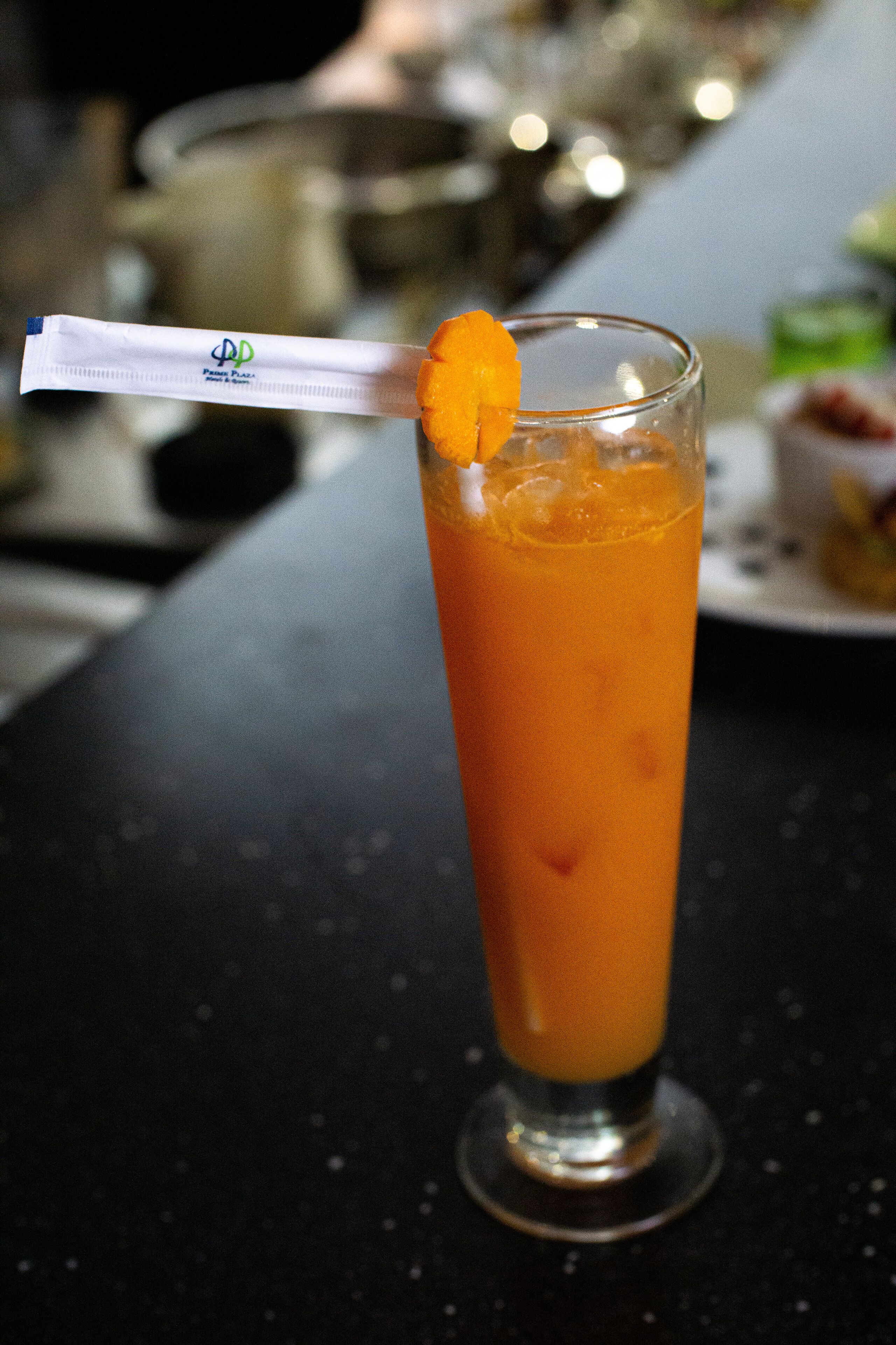 A tall glass with a straw and an orange garnish on a dark surface.