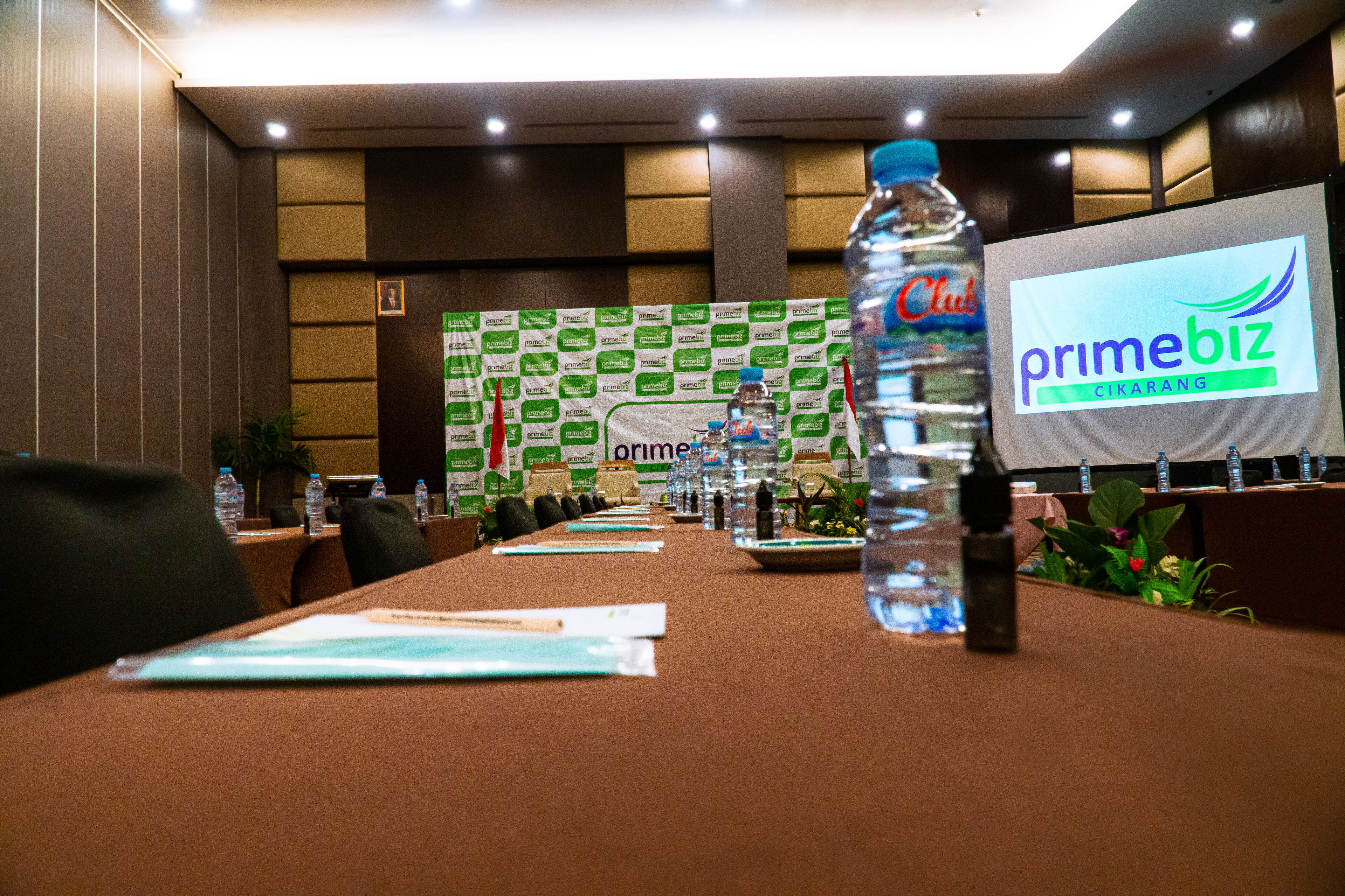 A conference room with a long table, water bottles, name tags, and a backdrop with logos.