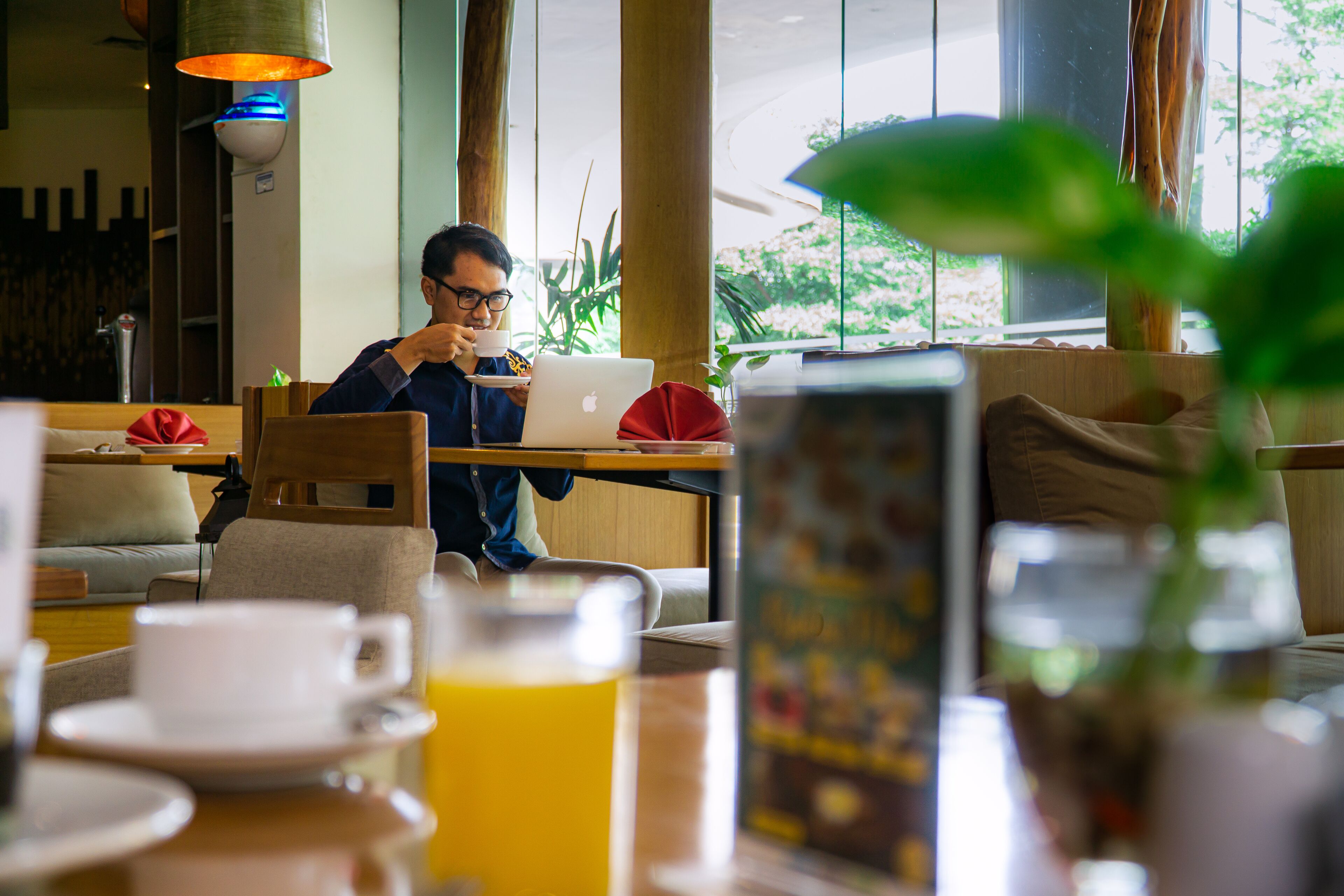 A man sitting at a table with a laptop, a cup, and a glass of orange juice.