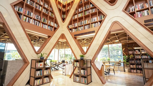 A modern library with geometric wooden bookshelves and a central open space with tables and chairs. - He Ti Hotel (Taichung)