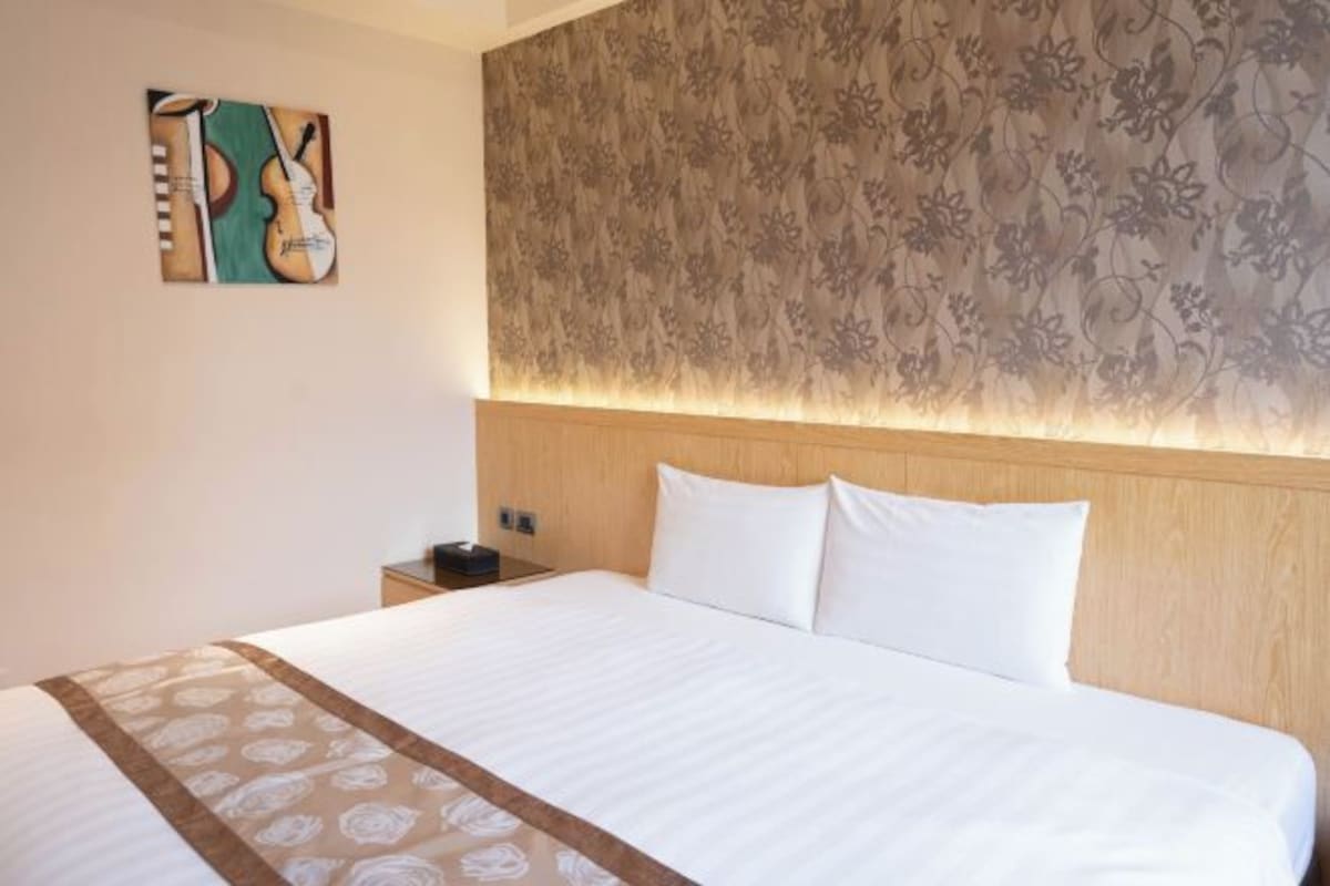 Habitación de hotel con una cama grande, cabecero de madera, pared con estampado floral y un cuadro de instrumentos musicales.