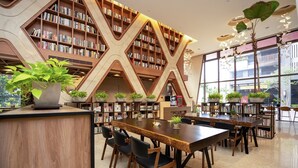 A modern library with wooden bookshelves, tables, chairs, and potted plants. - He Ti Hotel (Taichung)