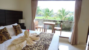 A hotel room with a bed, a wooden table, chairs, a balcony with a view of palm trees, and a stone wall. - Arnawa Bungalow (Ubud)