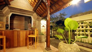 A wooden bar area with a stone pillar, a chair, and a large potted plant with broad leaves. - Arnawa Bungalow (Ubud)