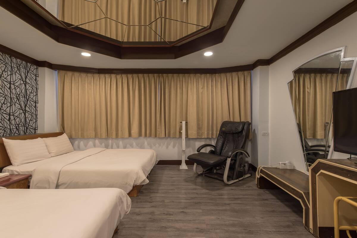 A hotel room with two beds, a desk, a chair, a TV, and a large window with curtains.