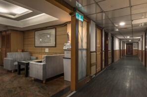 A hotel corridor with seating, a reception desk, and an exit sign.