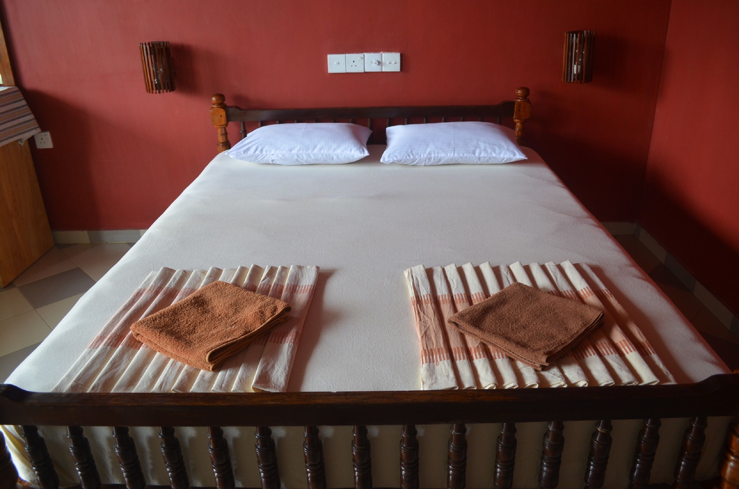 Una cama bien hecha con sábanas blancas y dos toallas marrones dobladas sobre ella.