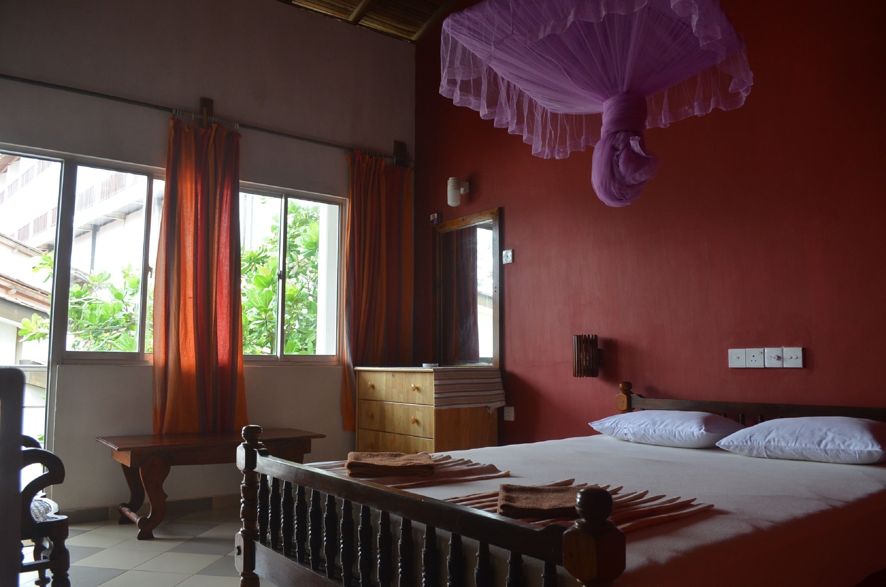 A bedroom with a bed, a wooden dresser, a window with curtains, and a purple canopy.