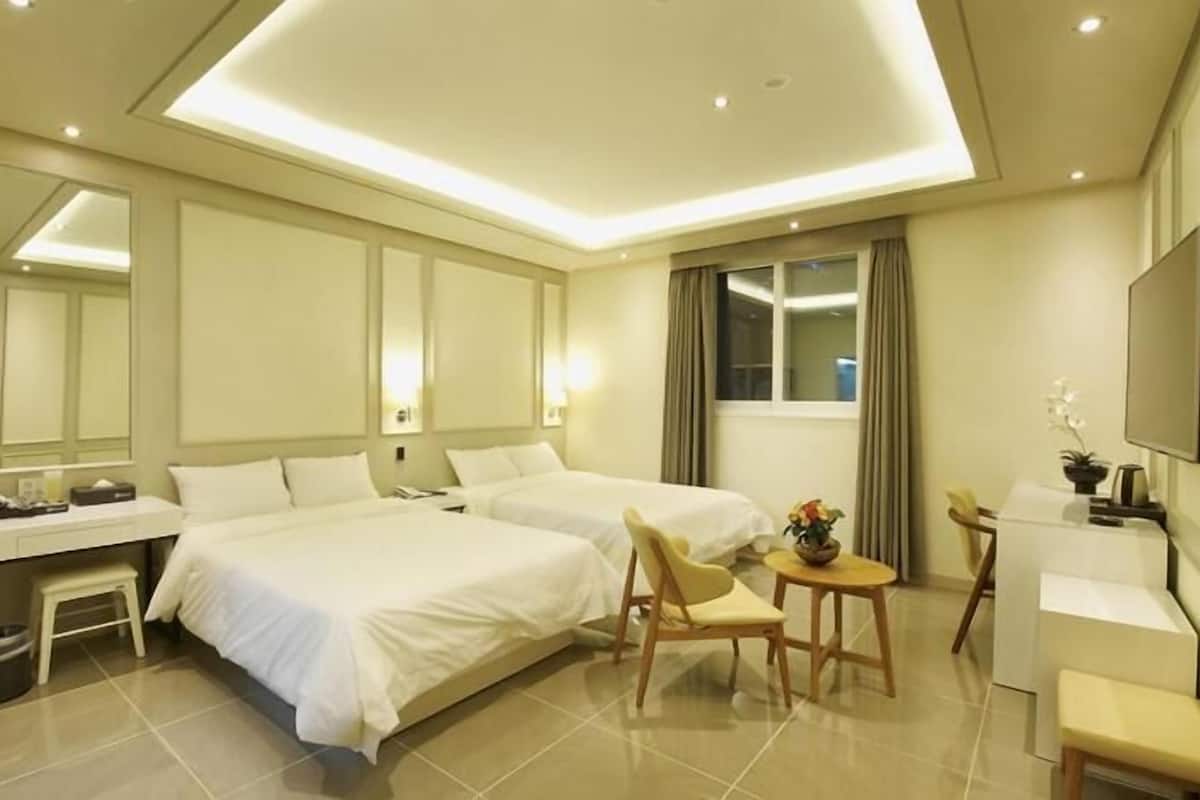 A hotel room with two beds, a desk, a chair, a TV, and a mirror.