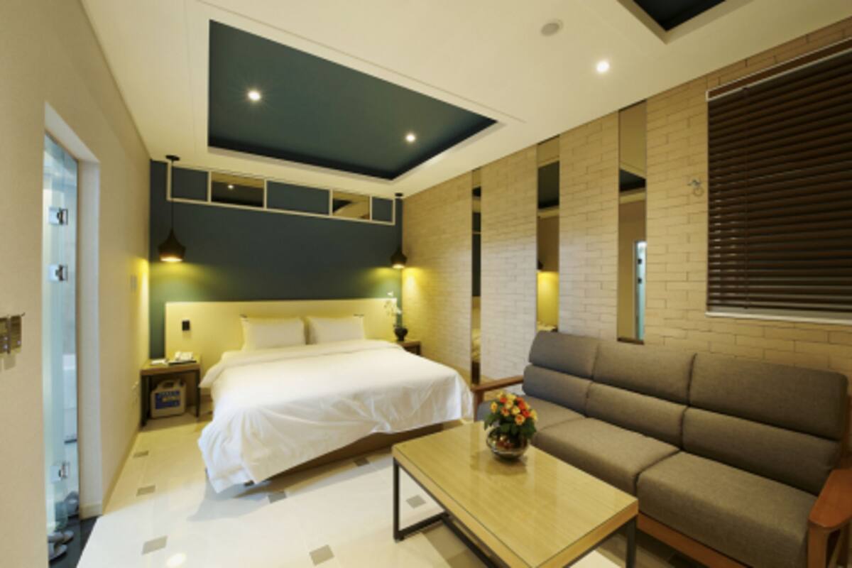 A modern hotel room with a large bed, a sofa, a coffee table, and a ceiling light fixture.