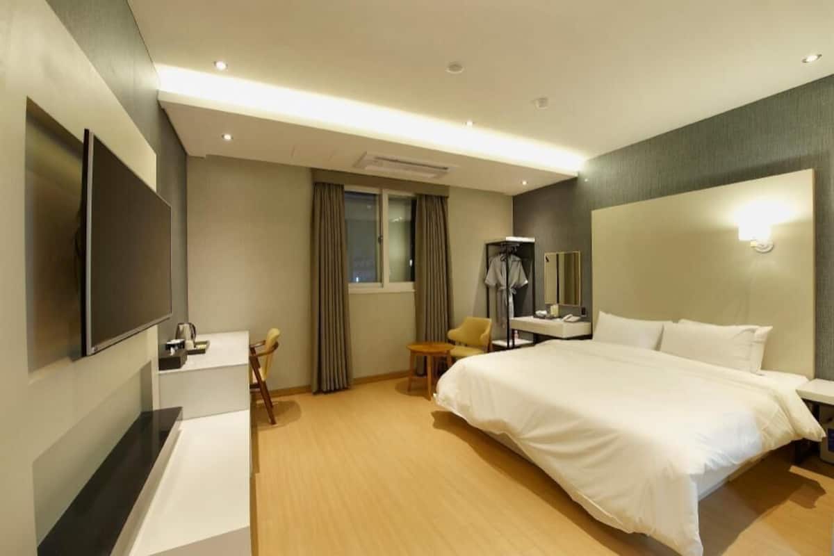 A hotel room with a bed, a desk, a chair, a TV, and a window with curtains.
