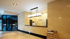 A hotel reception area with a modern design, featuring a reception desk, a digital screen, and a signboard with hotel amenities. - Hotel B (Gwangju)
