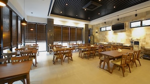 A spacious dining area with multiple wooden tables and chairs, a kitchen area with a large stove and a flat-screen TV mounted on the wall. - Hotel B (Gwangju)