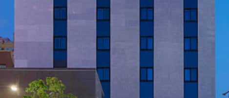 A modern hotel building with a prominent 'HOTEL B' sign, multiple floors, and a well-lit facade.
