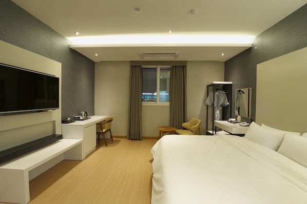 A hotel room with a bed, a desk, a chair, a TV, and a window with curtains.