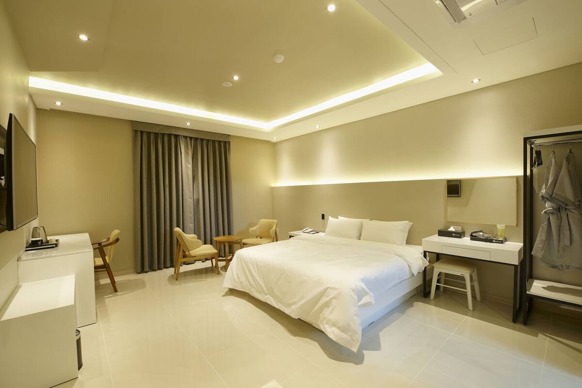 A modern hotel room with a large bed, a desk, a chair, a TV, and a bathroom.