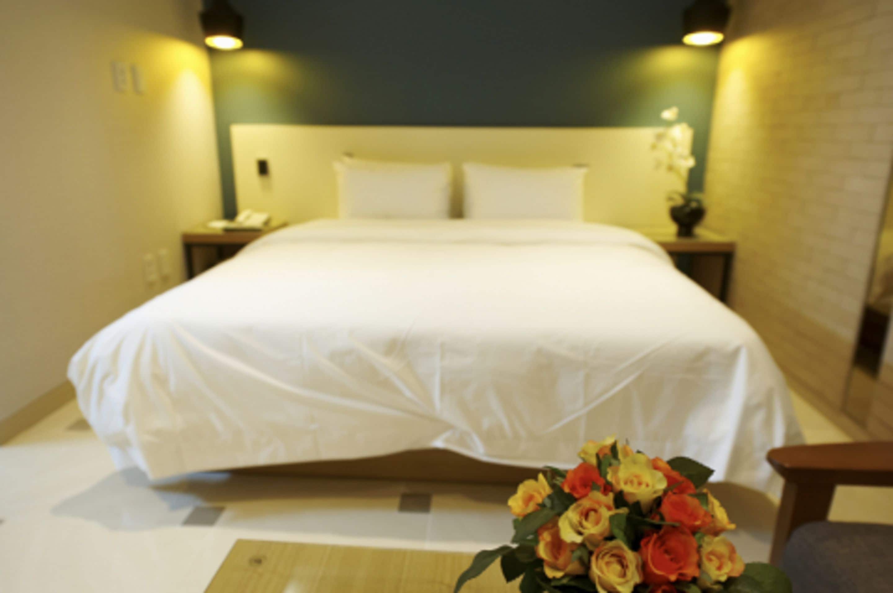 A hotel room with a large bed, bedside tables, a nightstand, and a bouquet of flowers on the floor.