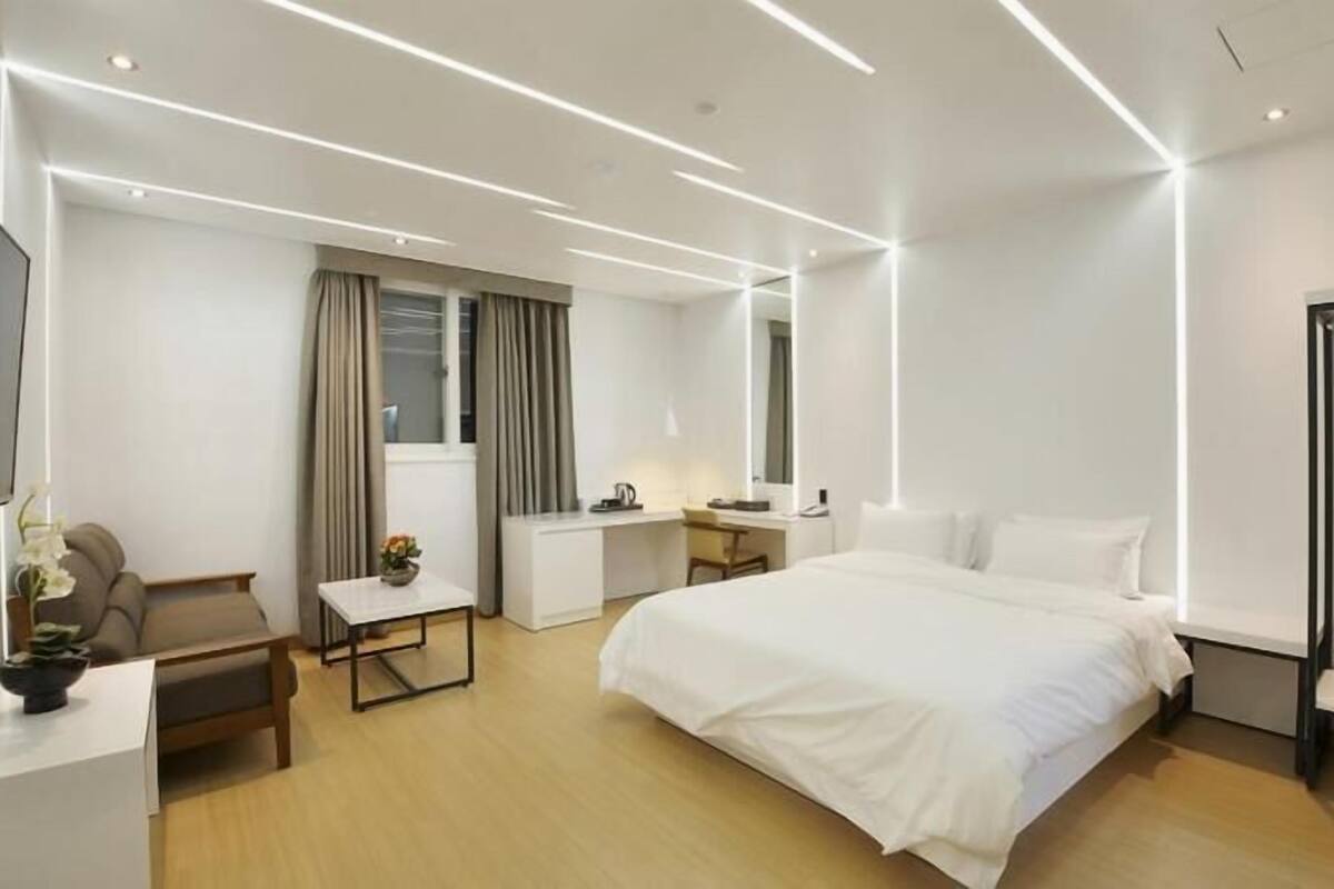 A modern hotel room with a bed, desk, chair, and wardrobe.