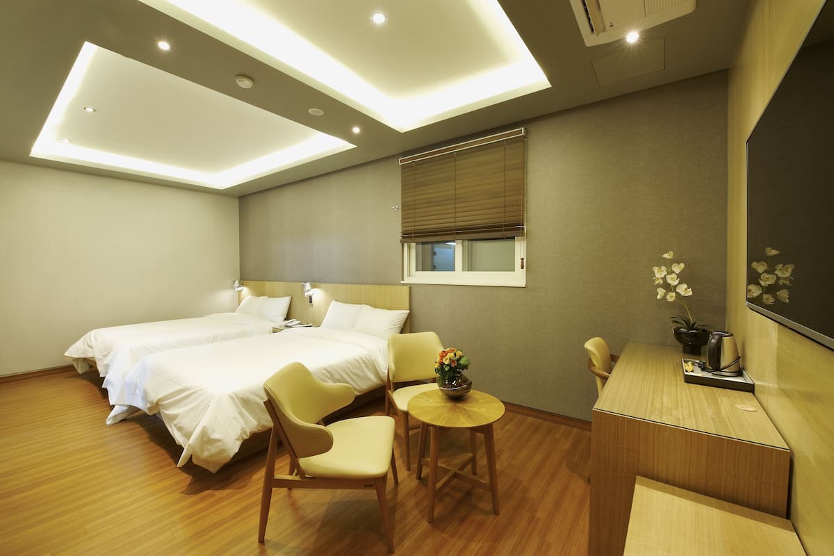 A hotel room with two beds, a small table with a flower vase, a chair, and a desk with a mirror.