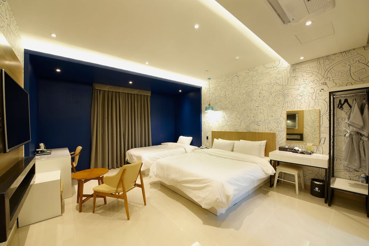 A hotel room with two beds, a desk, a chair, a vanity with a mirror, and a television.