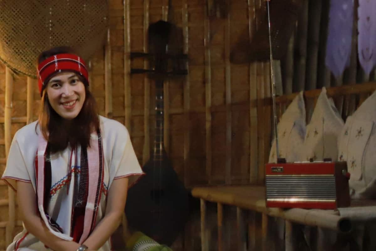 A rustic interior with wooden walls, a large woven basket, a guitar, and a radio on a table.