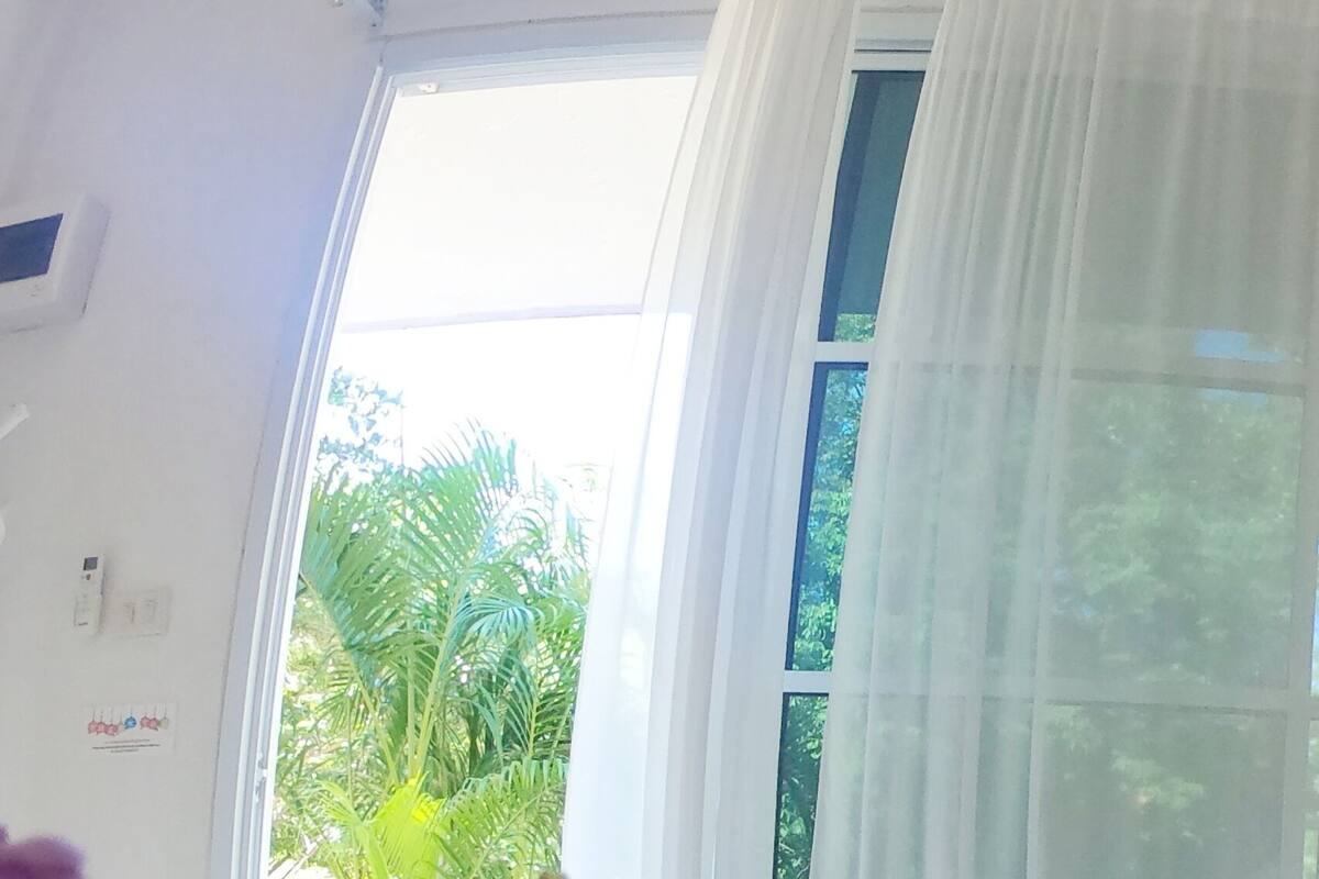 A room with a large window, a colorful abstract painting on the wall, and a view of greenery outside.