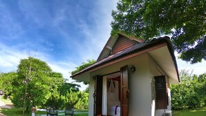 A small house with a tiled porch, a wooden door, and a small air conditioning unit on the side.