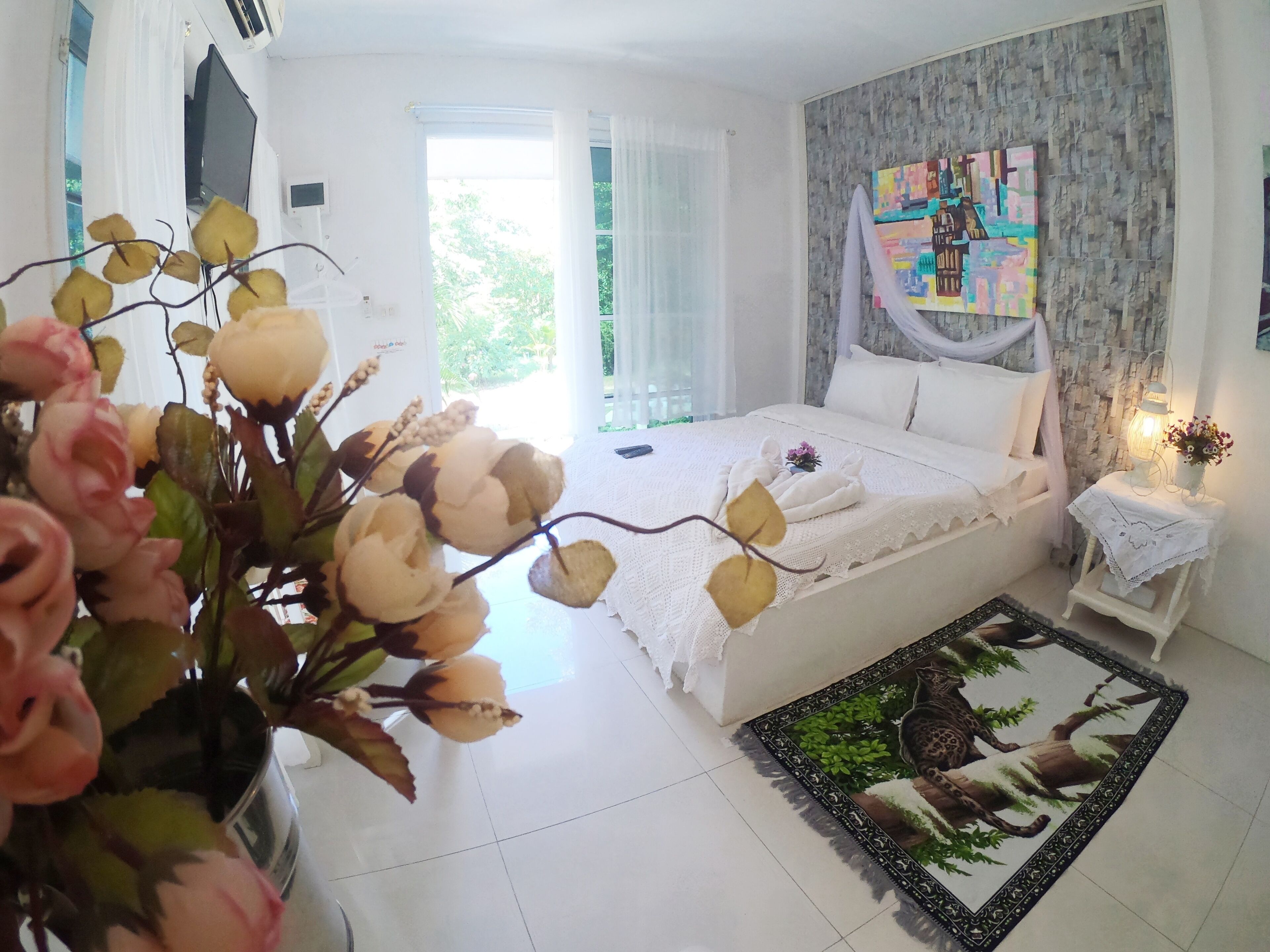 A bedroom with a bed, a bedside table with a lamp, a window with curtains, and a wall with a textured pattern.