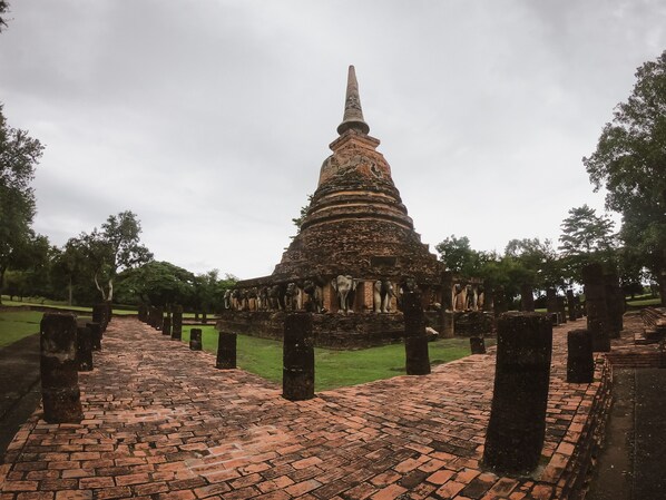 Un temple històric amb una estructura escalonada i una agulla apuntada, envoltat d'un camí de rajola i arbres.