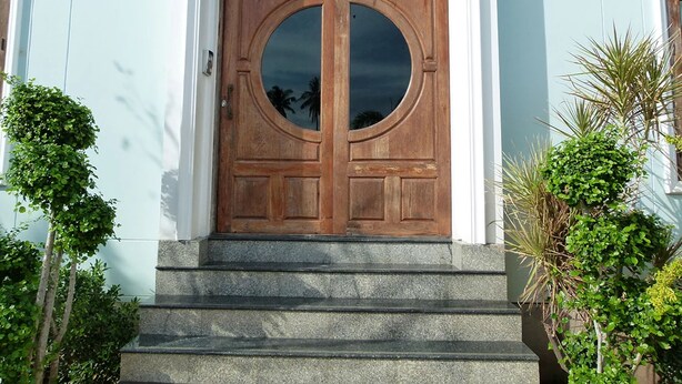 A wooden double door with a circular window, set in a light blue building with stone steps leading up to it.