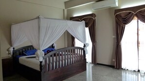 A bedroom with a four-poster bed, a ceiling fan, and a large window with curtains.