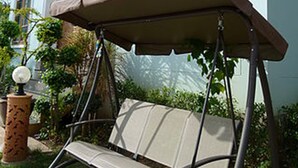 A light blue building with a swing seat under a brown canopy.