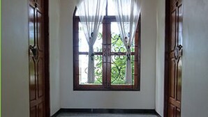 A hallway with a polished floor, a large window with a metal grill, and wooden doors.