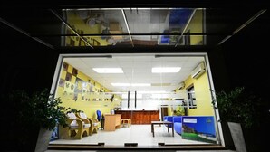 Een receptie met een incheckbalie, een zithoek met stoelen en een glazen wand.