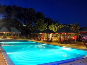 A swimming pool with lounge chairs and umbrellas, surrounded by trees and covered structures. - Laya Leisure (Palindanuwara)