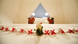 Een bed met een witte lakenset, een enkele roos en rode decoratieve accenten.