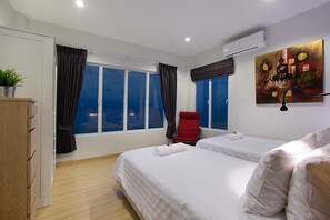 Une chambre d’hôtel avec deux lits, un fauteuil rouge, une grande fenêtre avec des rideaux, un tableau au mur et un appareil de climatisation.