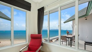 Una habitación con una silla roja, ventanas amplias y vista a la playa y al océano.
