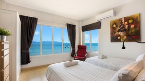 Habitación de hotel con dos camas, una silla roja, un cuadro y vista al mar.