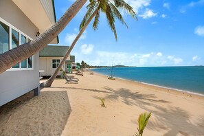 Une plage avec un palmier, un bâtiment avec une porte verte et un ciel bleu clair.