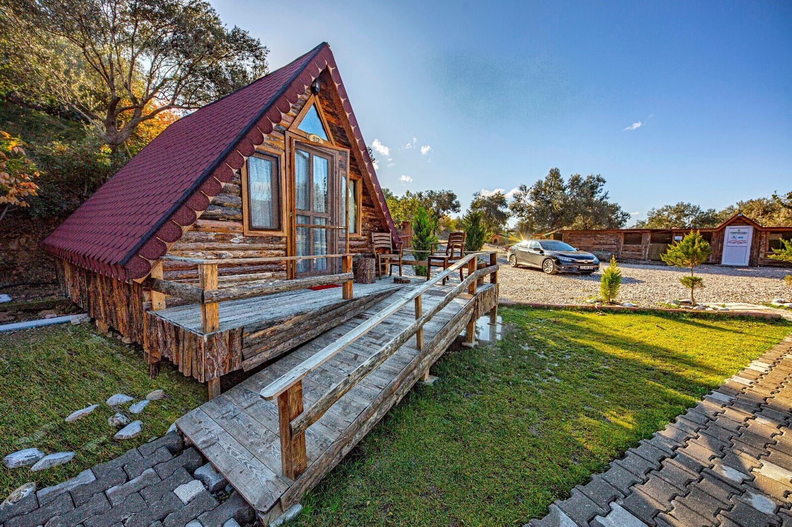 A rustic log cabin with a red roof, a wooden porch, and a gravel driveway.