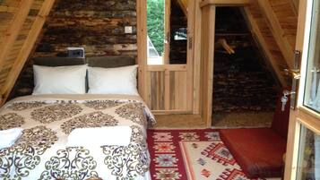A cozy attic bedroom with a bed, a wooden door, and a view of the outdoors.