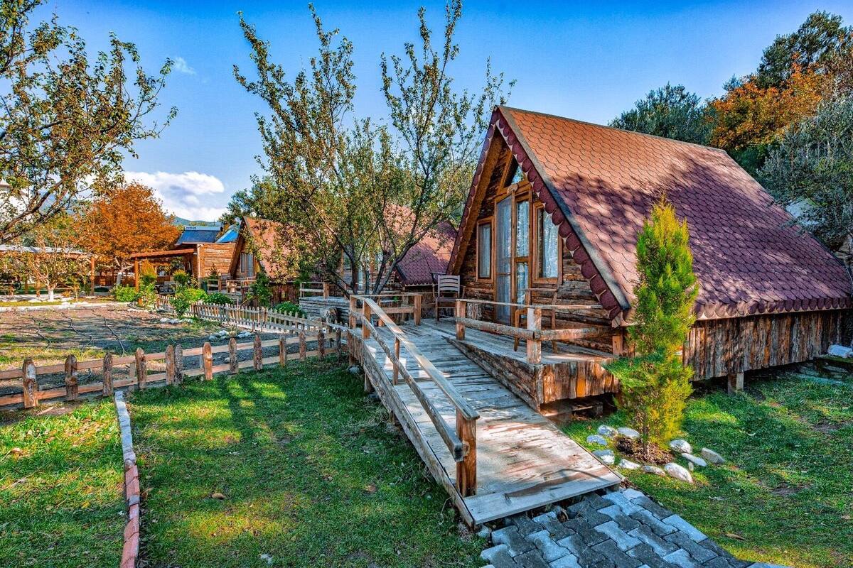 Une cabane rustique en rondins de bois, dotée d’une terrasse en bois et d’un toit de chaume.