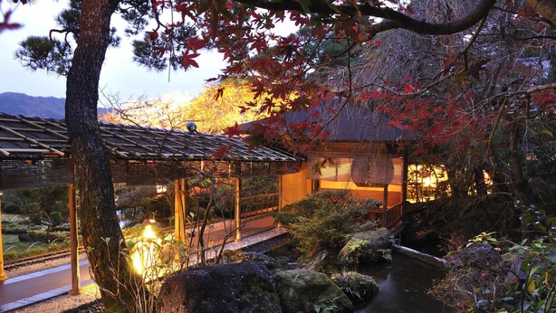 A traditional Japanese garden with a wooden structure, a pond, and autumn foliage. - Atami Taikansou (Atami)
