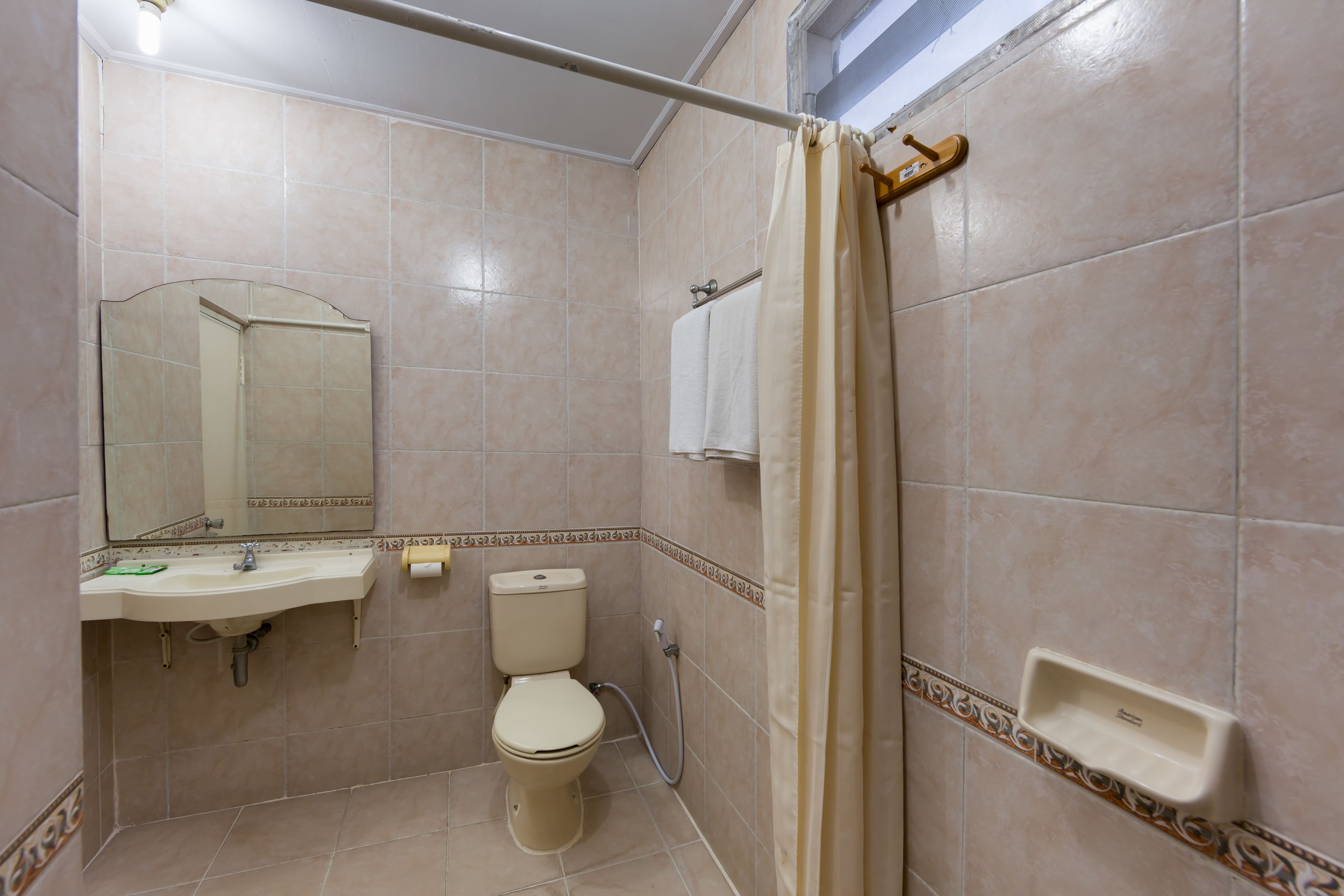 Un baño con lavamanos, inodoro, espejo, cortina de ducha y toallero.