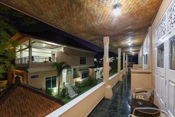A hotel corridor with a covered walkway, outdoor seating area, and a staircase leading to a second floor.