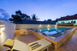 A swimming pool with lounge chairs and a tiled deck area.